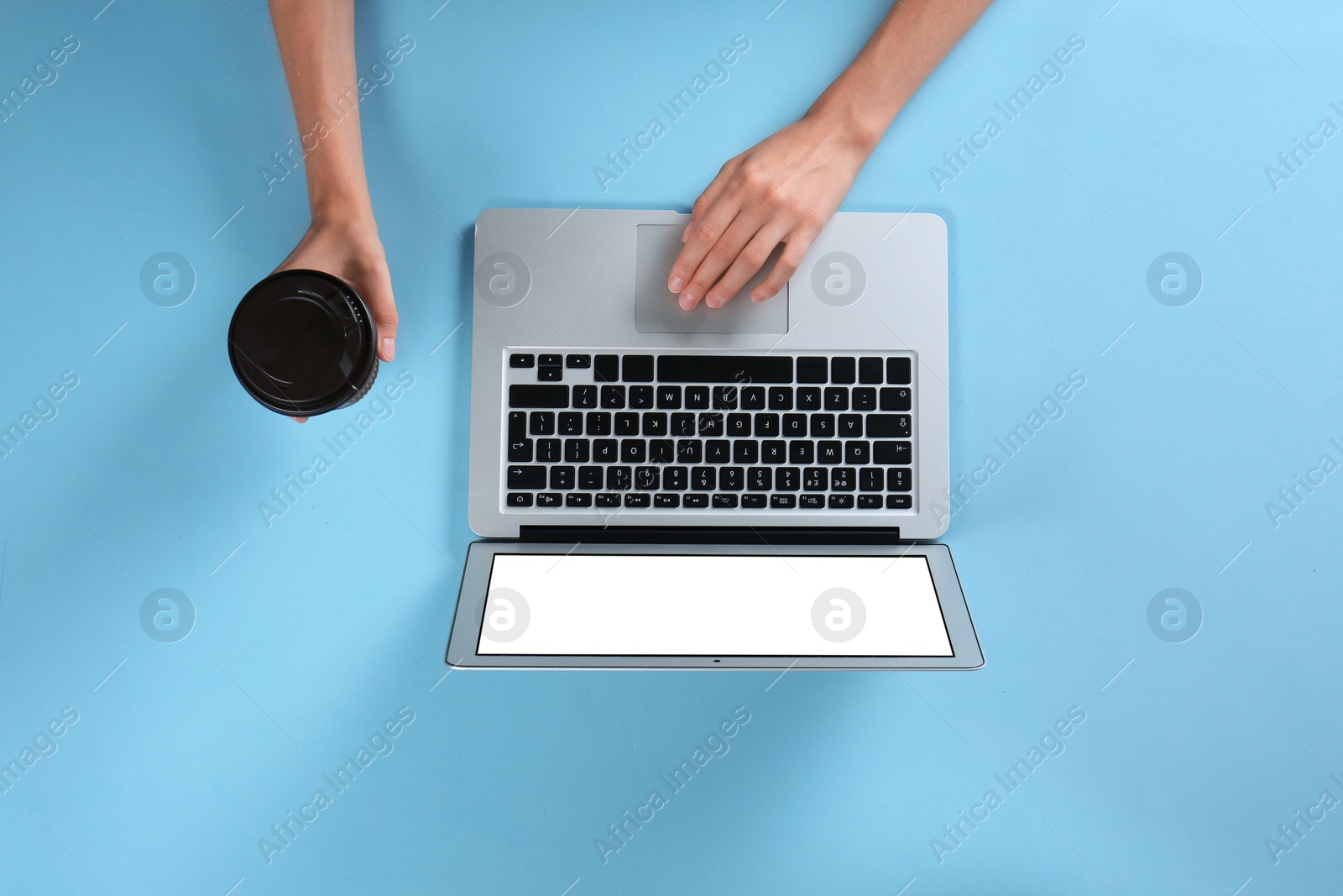 Photo of Young woman holding coffee while using laptop on light blue background, top view