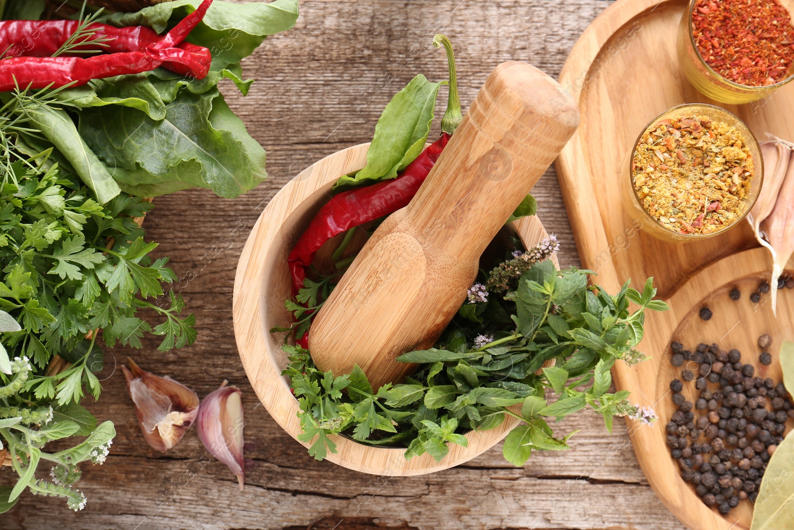 Photo of Mortar with pestle, fresh green herbs and different spices on wooden table, flat lay