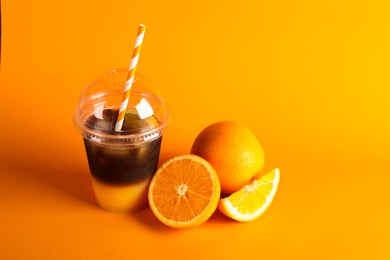 Photo of Tasty refreshing drink with coffee and orange juice in plastic cup on bright color background