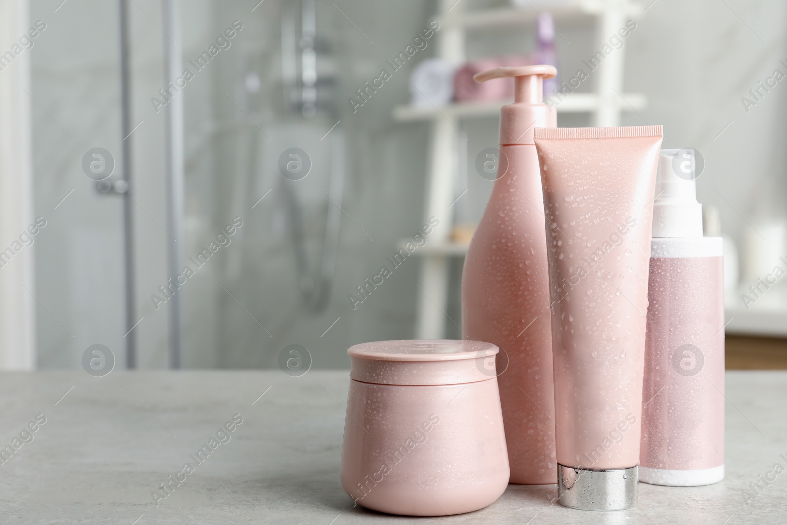 Photo of Set of hair care cosmetic products covered with water drops on light grey stone table in bathroom. Space for text