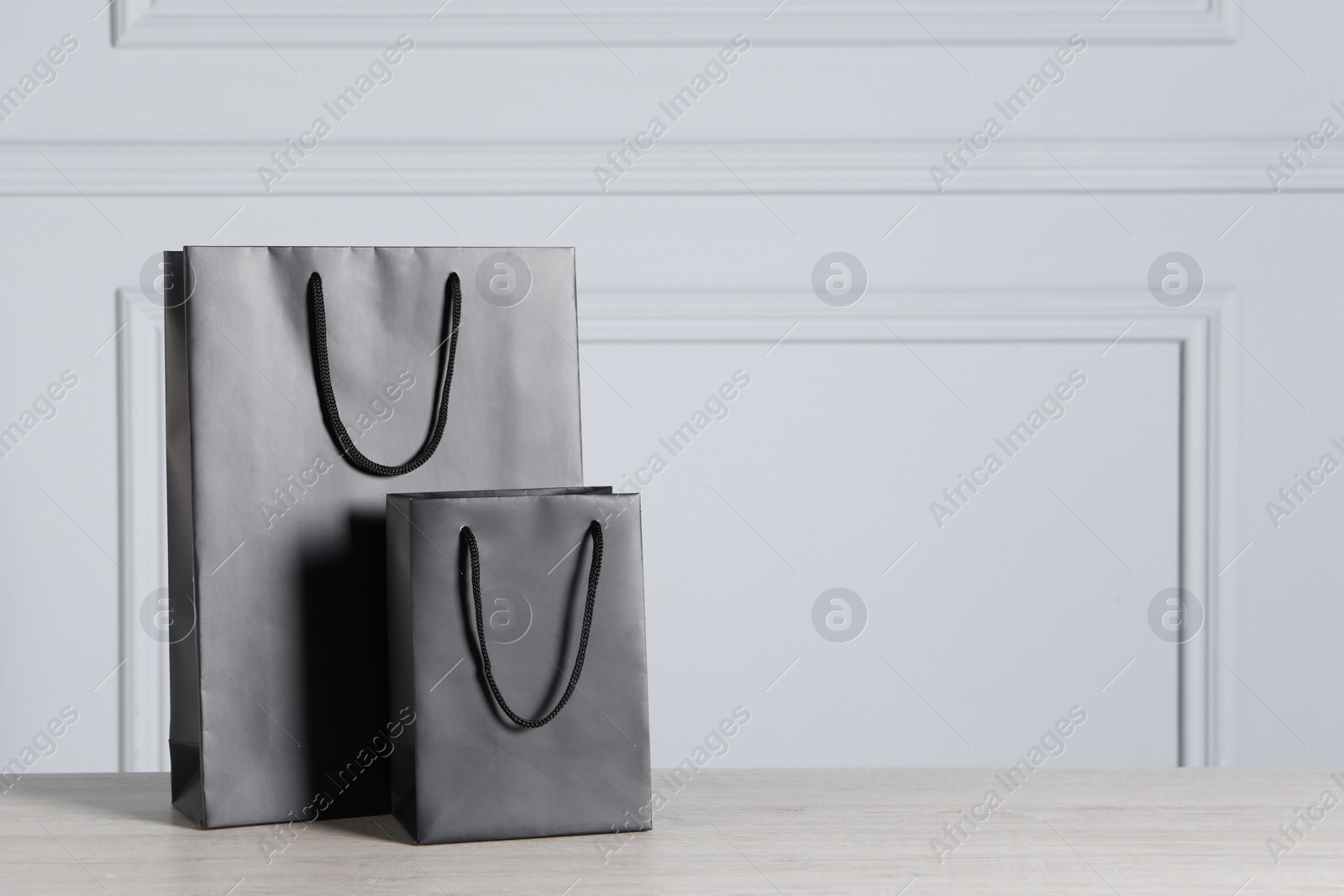 Photo of Black paper bags on wooden table against light grey wall, space for text