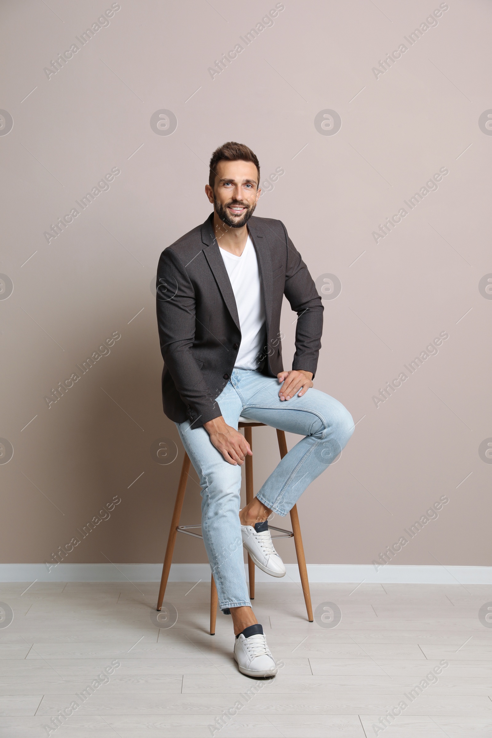 Photo of Handsome man sitting on stool near beige wall