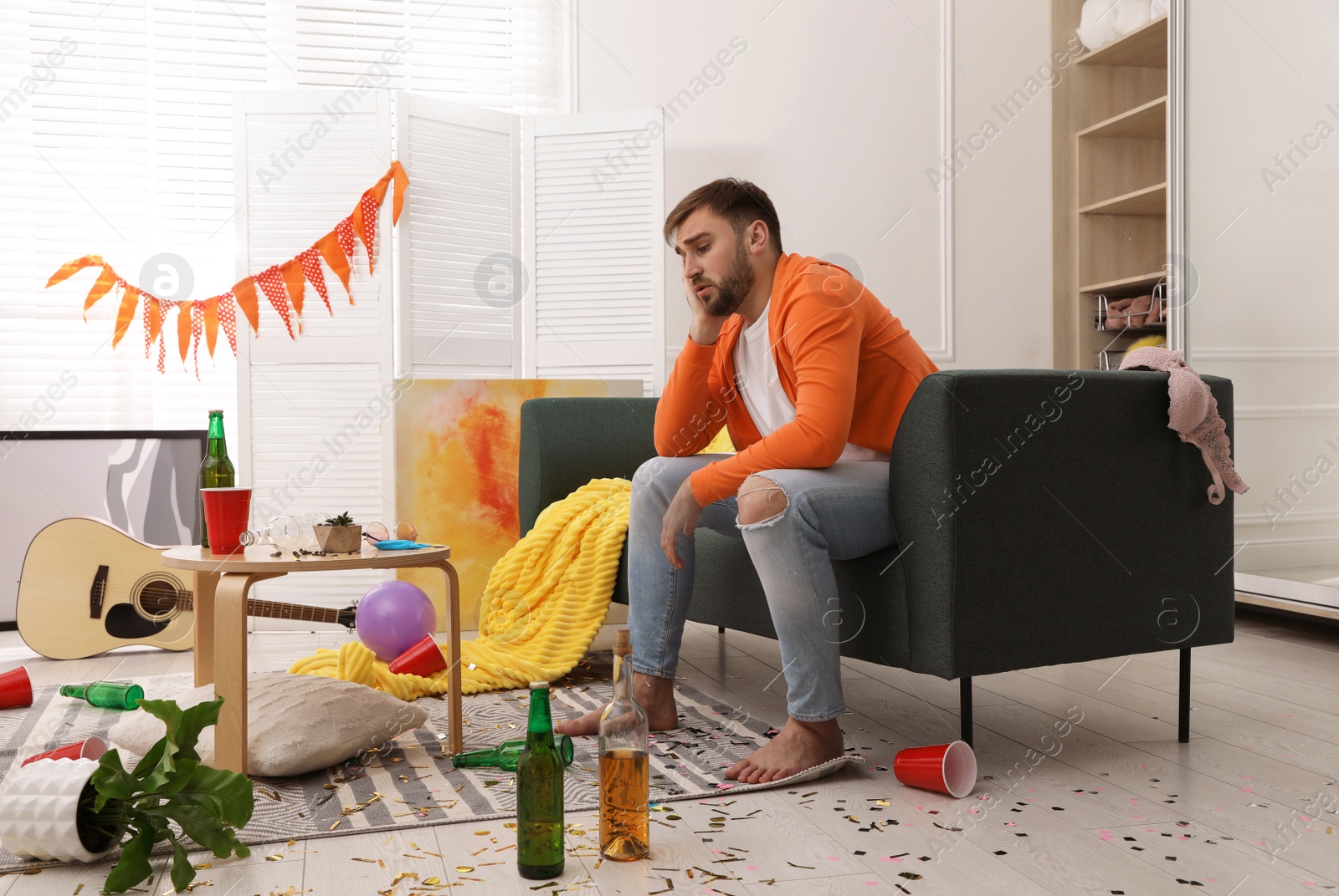 Photo of Tired drunk man on sofa in messy room after party