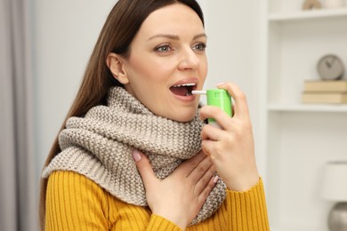 Photo of Adult woman with scarf using throat spray at home