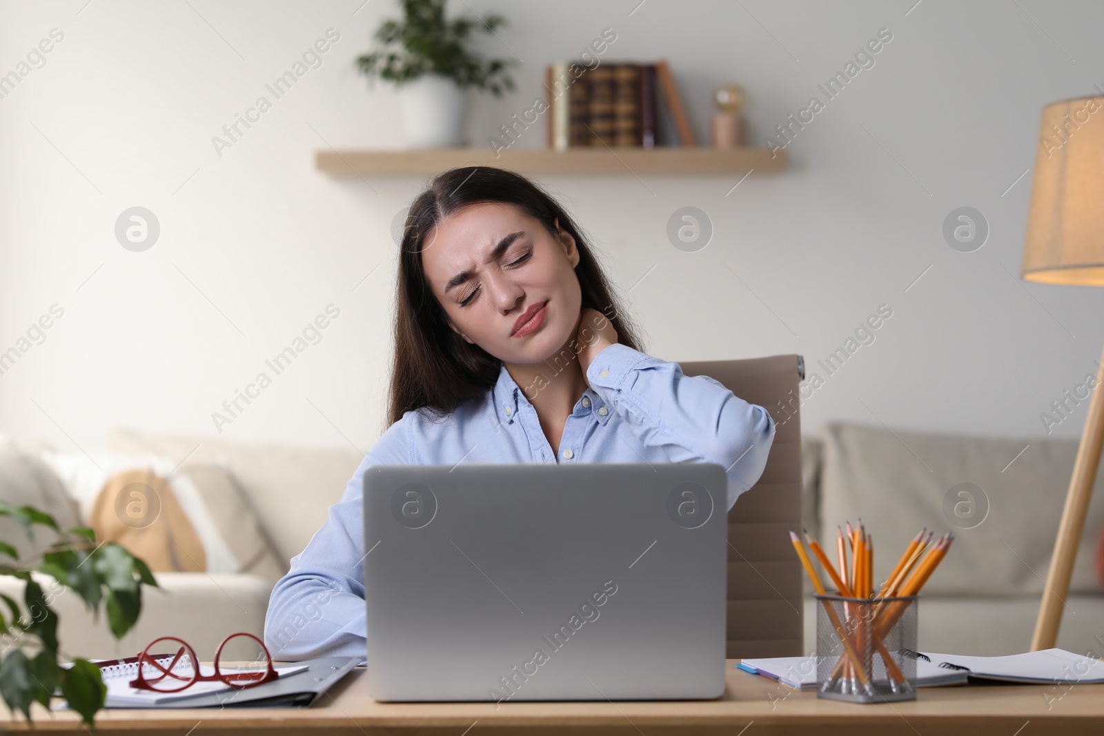 Photo of Young woman suffering from neck pain at table in office