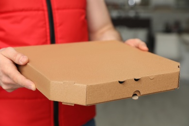 Photo of Man with pizza box indoors, closeup. Food delivery service