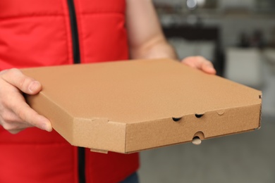 Man with pizza box indoors, closeup. Food delivery service