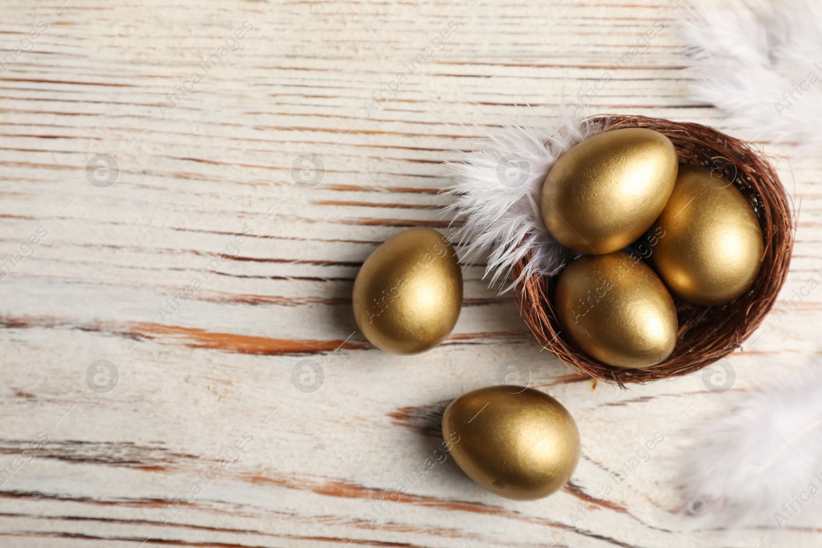 Photo of Nest with golden eggs on white wooden table, flat lay. Space for text