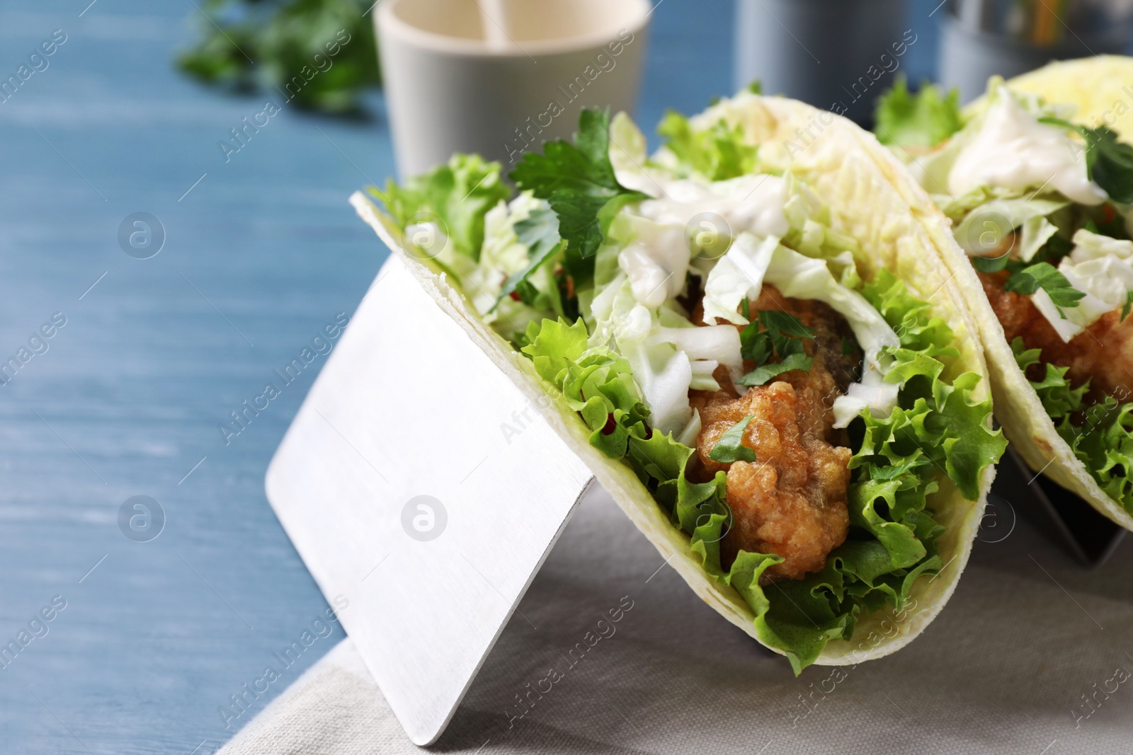 Photo of Yummy fish tacos in holder on blue wooden table, closeup