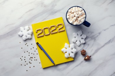 Photo of Stylish planner, cup of tasty hot drink and Christmas decor on white marble background, flat lay. 2022 New Year aims