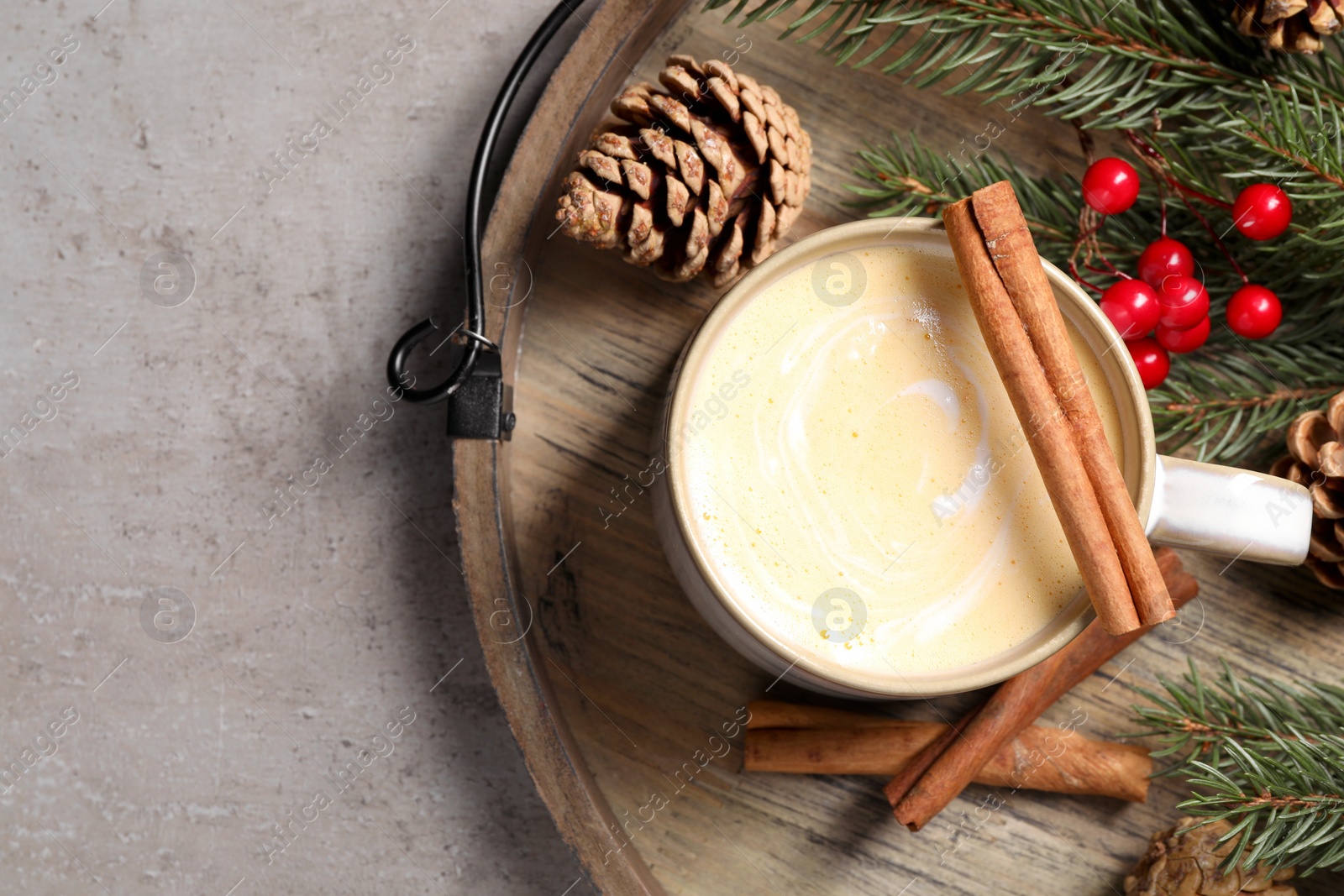 Photo of Tasty eggnog, cinnamon sticks and fir branches on grey textured table, top view. Space for text