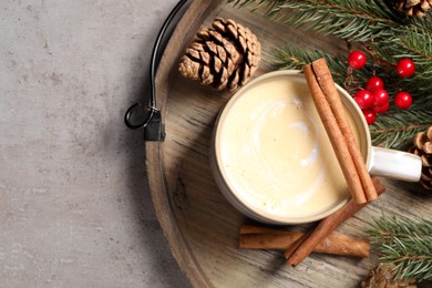 Photo of Tasty eggnog, cinnamon sticks and fir branches on grey textured table, top view. Space for text