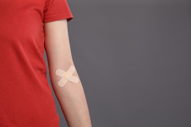 Blood donation. Woman with sticking plaster on her arm against grey background, closeup. Space for text