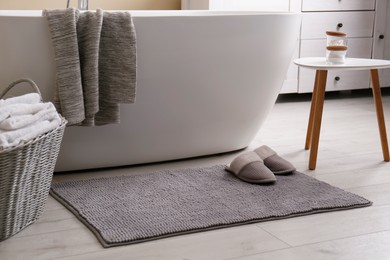 Soft grey mat with slippers on floor near tub in bathroom. Interior design