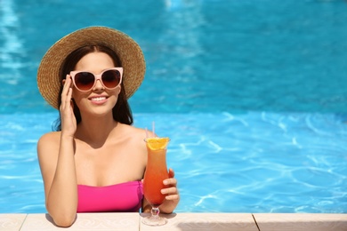 Photo of Beautiful young woman with cocktail in blue swimming pool