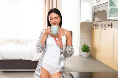 Photo of Beautiful young woman in white underwear drinking coffee at home