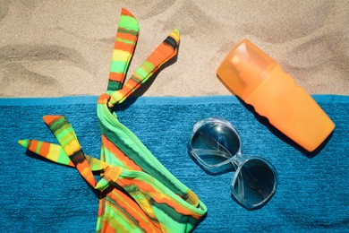Soft blue beach towel with bottle of sunscreen, sunglasses and colorful bikini bottom, flat lay