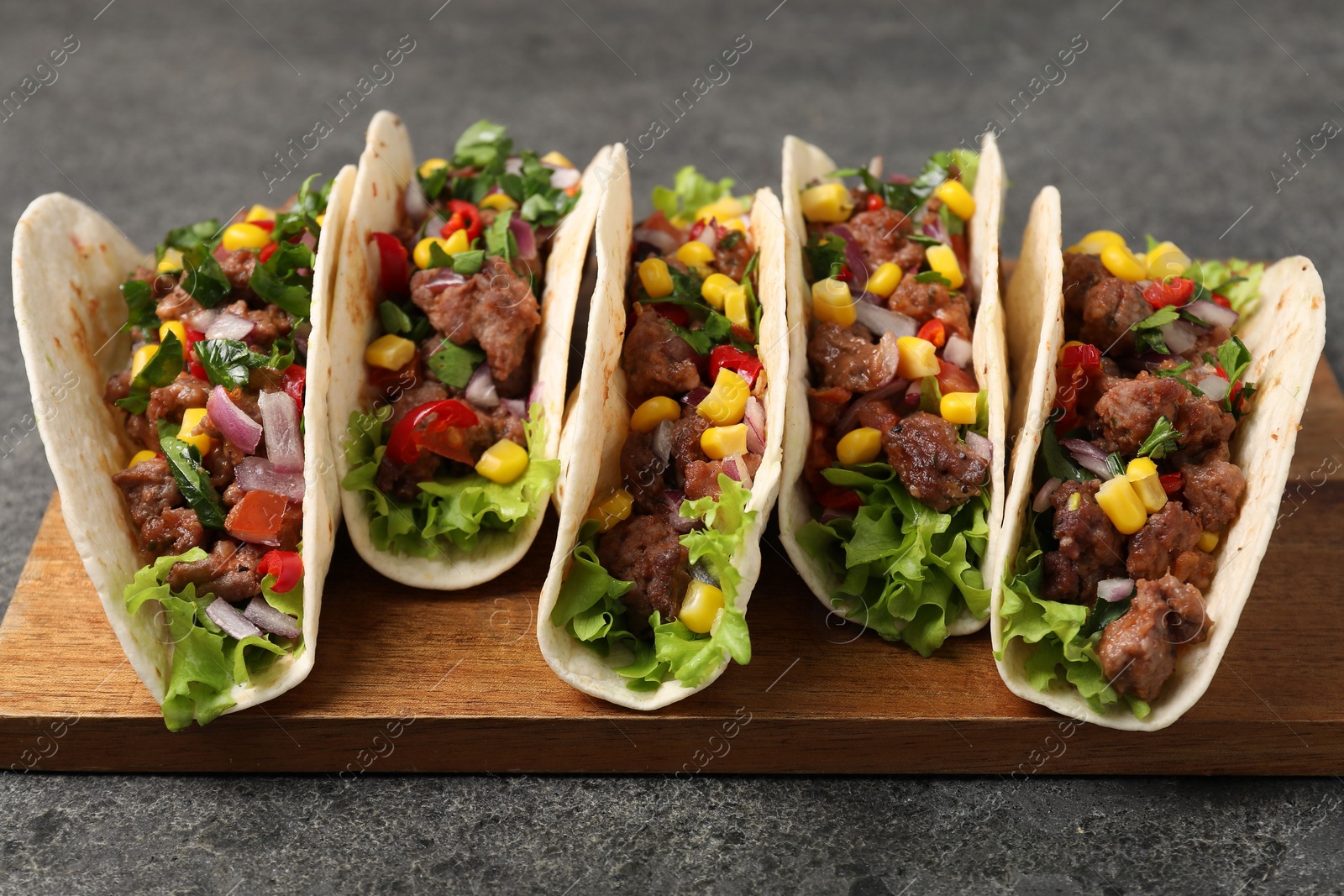 Photo of Delicious tacos with meat and vegetables on gray textured table