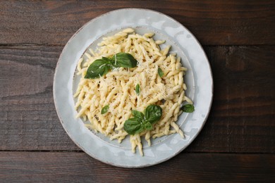 Plate of delicious trofie pasta with cheese and basil leaves on wooden table, top view