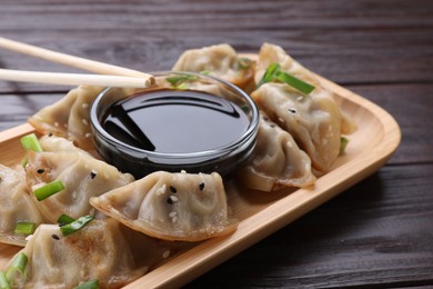 Photo of Delicious gyoza (asian dumplings) with green onions, soy sauce and chopsticks on wooden table, closeup