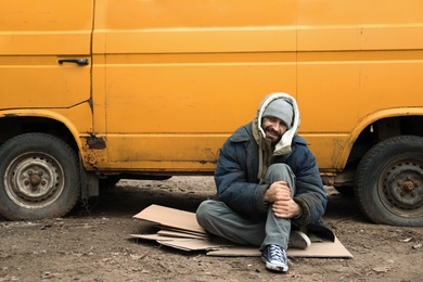 Photo of Poor homeless man sitting near van outdoors