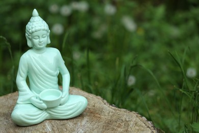 Decorative Buddha statue on stump outdoors, space for text