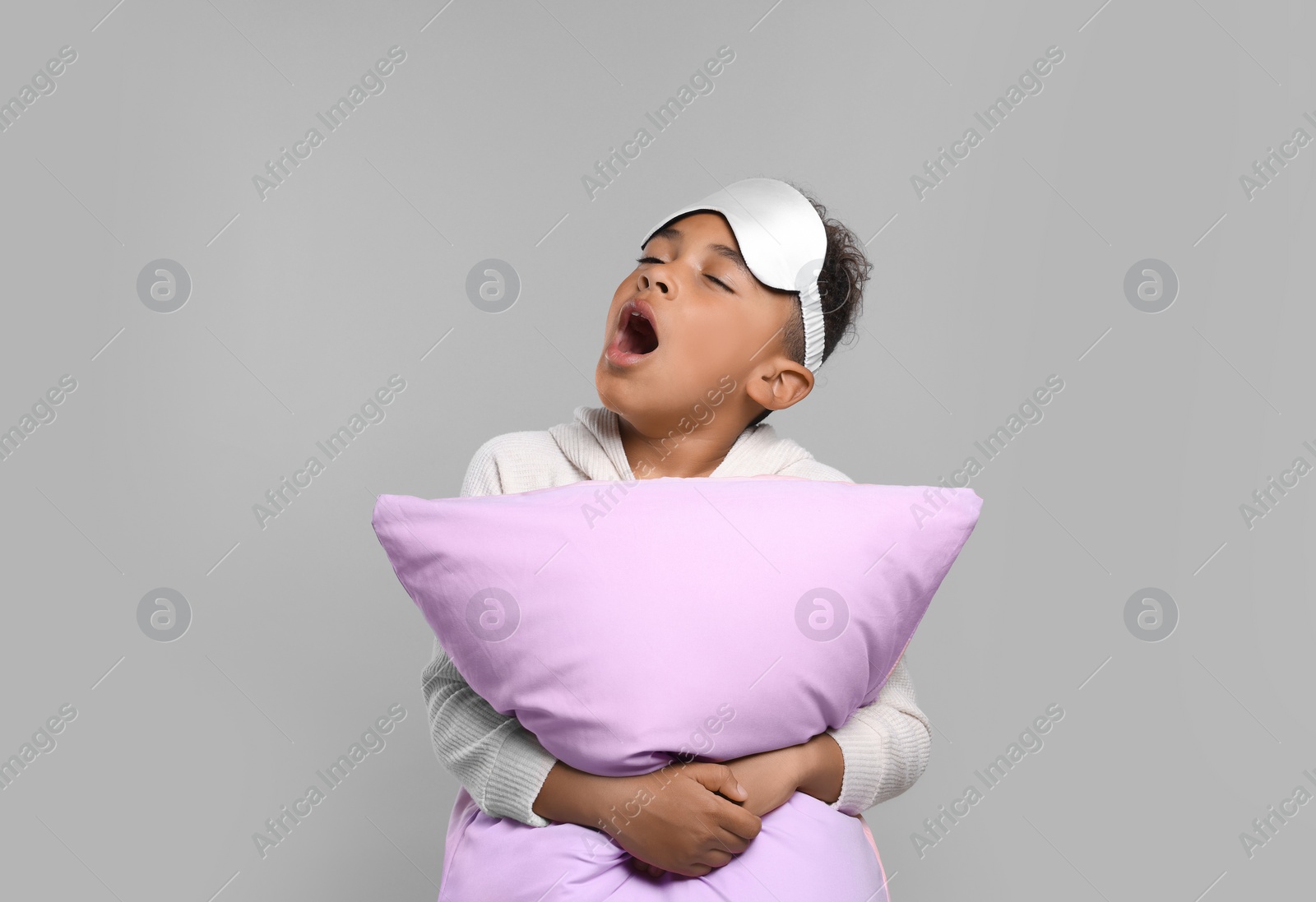 Photo of Boy with pillow and sleep mask yawning on grey background. Insomnia problem