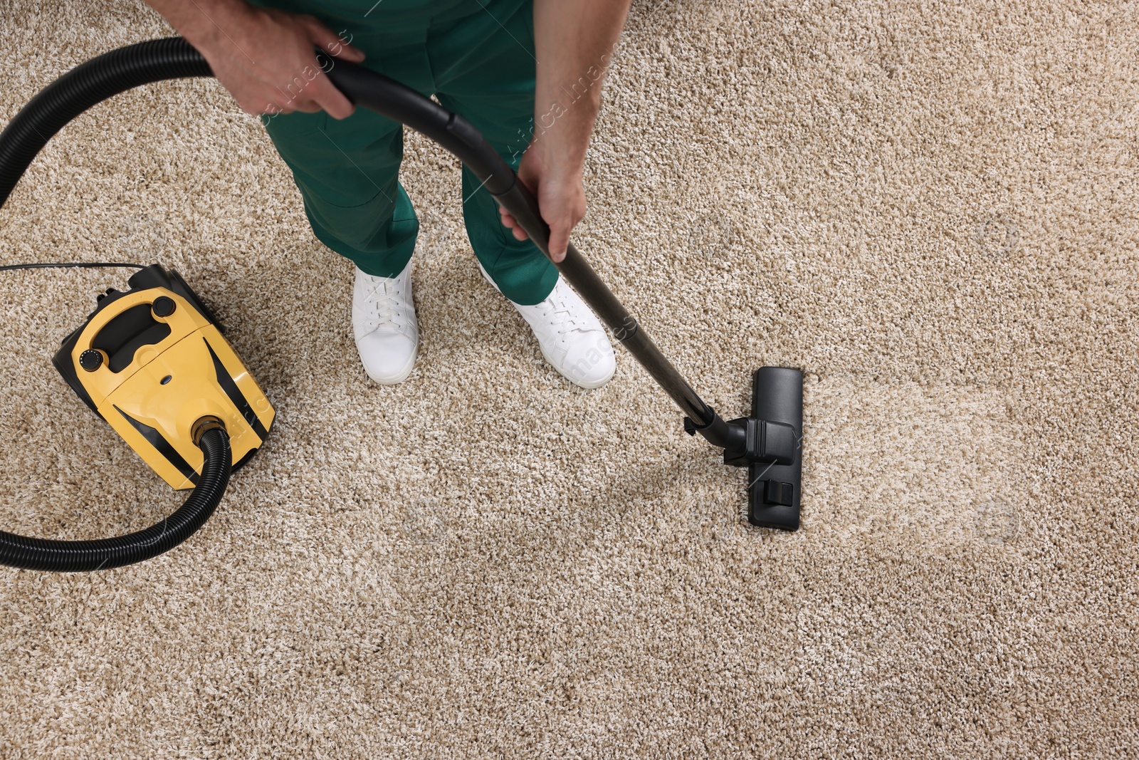 Photo of Dry cleaner's employee hoovering carpet with vacuum cleaner, above view