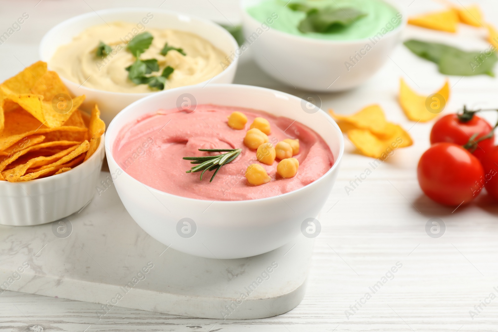 Photo of Different kinds of tasty hummus, nachos and ingredients on white wooden table