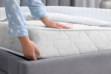 Photo of Woman putting new soft mattress on grey bed, closeup
