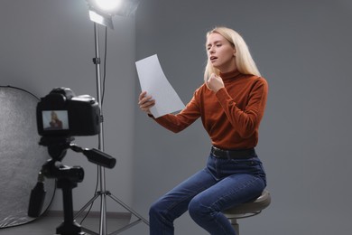 Photo of Casting call. Emotional woman with script sitting on chair and performing in front of camera in studio