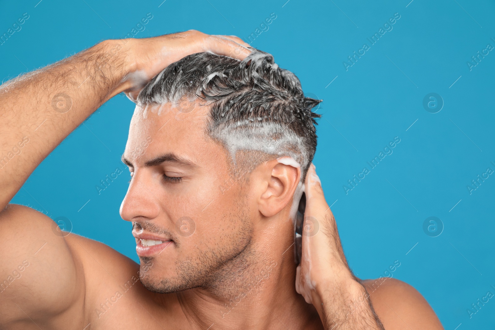 Photo of Handsome man washing hair on light blue background