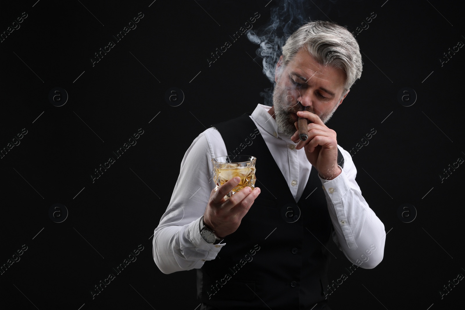 Photo of Bearded man with glass of whiskey smoking cigar against black background. Space for text