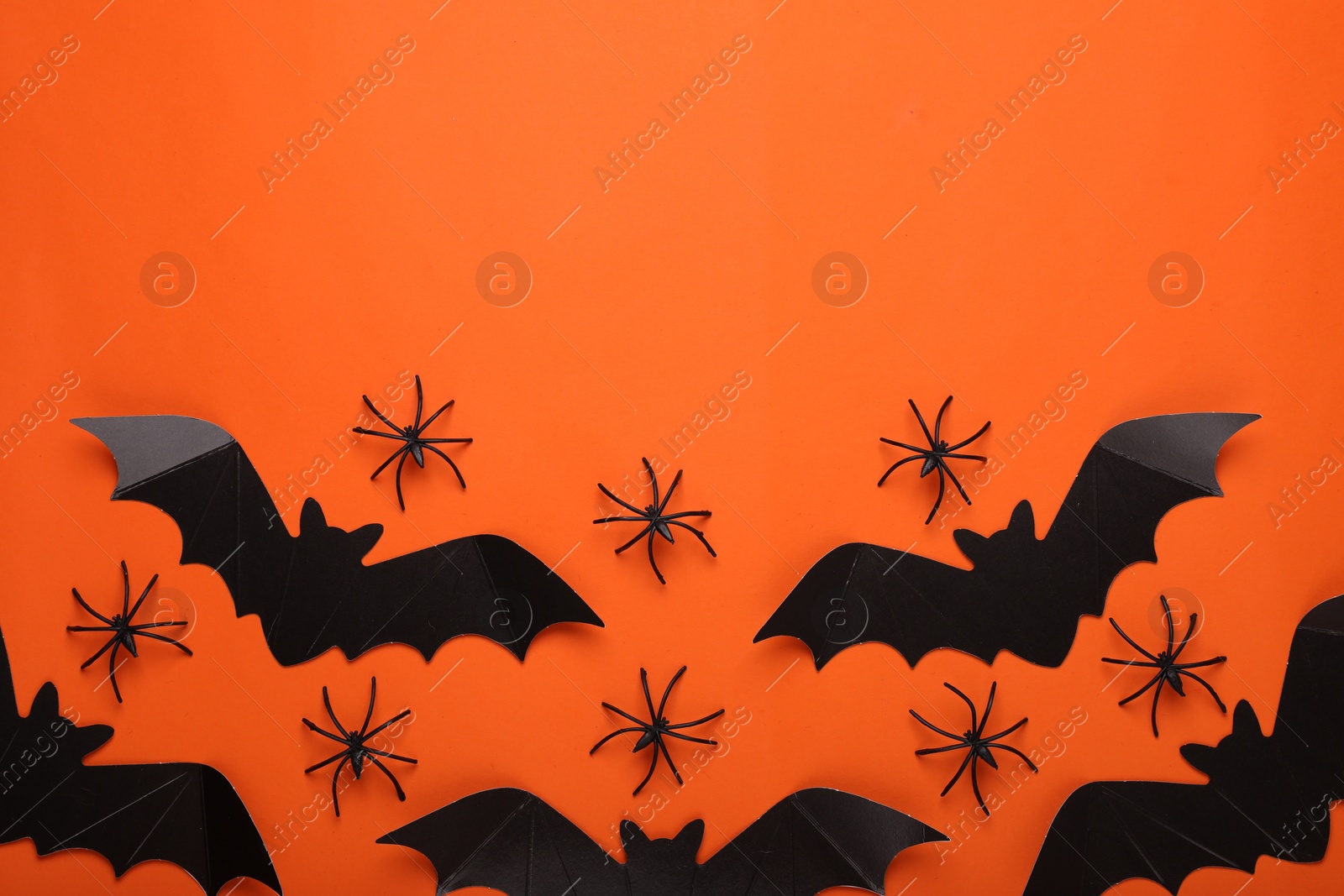 Photo of Flat lay composition with paper bats and spiders on orange background, space for text. Halloween celebration