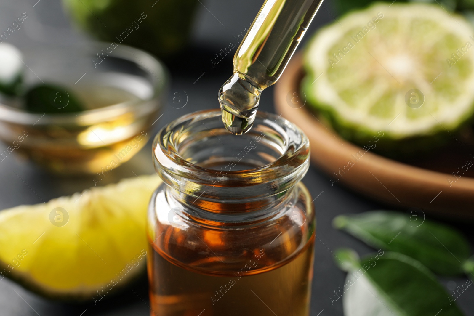 Photo of Bergamot essential oil dripping from pipette into bottle on table, closeup