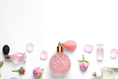 Different perfume bottles and flowers on white background, top view