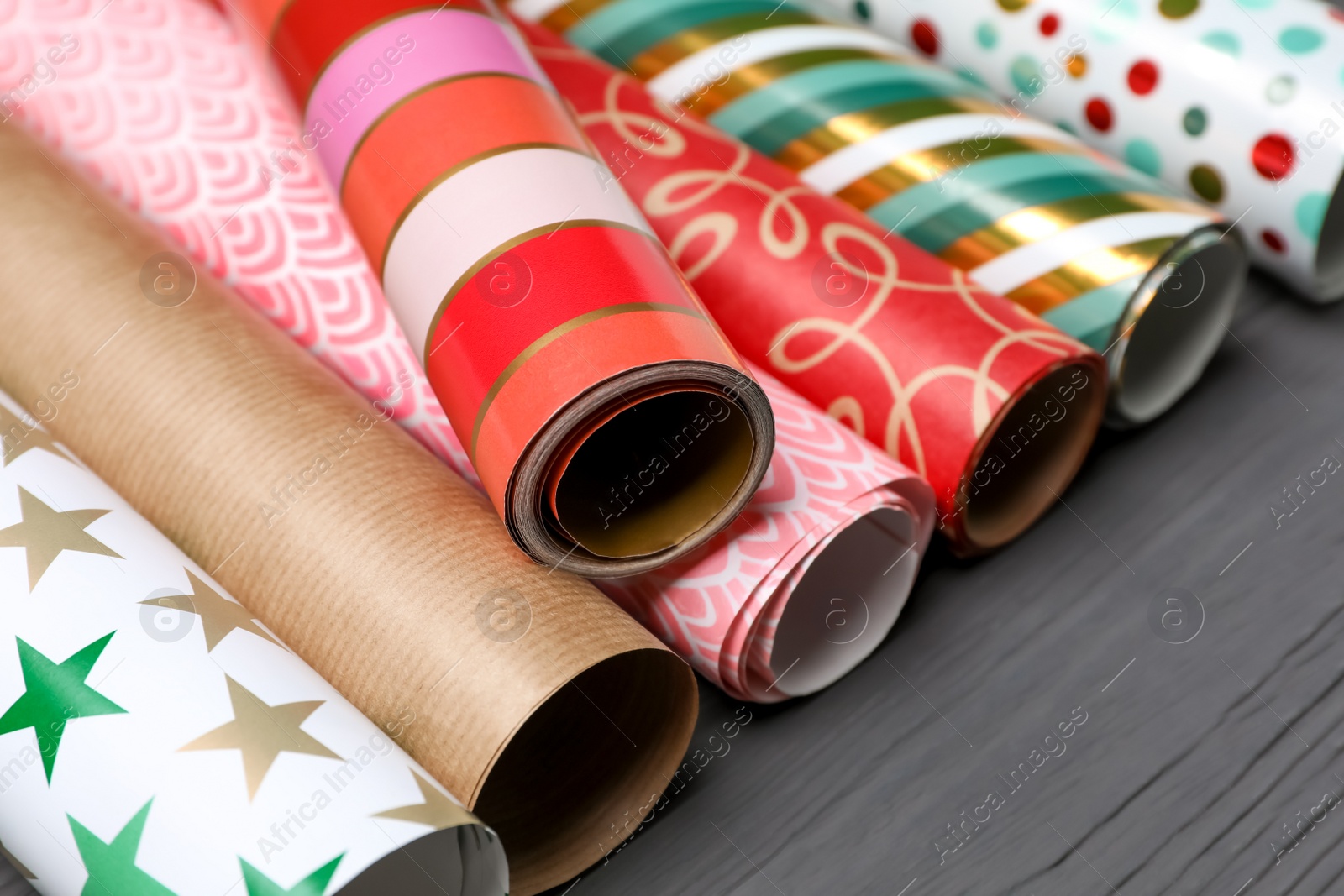 Photo of Different colorful wrapping paper rolls on grey wooden table, closeup