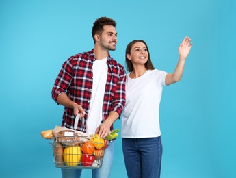 Young couple with shopping basket full of products on blue background