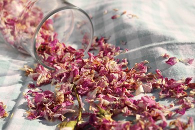 Photo of Glass bottle with scattered dried tea rose flowers and petals on checkered fabric, closeup
