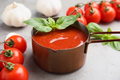 Photo of Pan of tasty tomato sauce with basil served on grey table