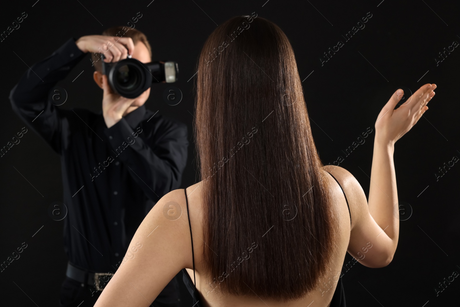 Photo of Professional photographer taking picture of model on black background, selective focus