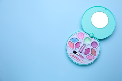 Decorative cosmetics for kids. Eye shadow palette with lipstick on light blue background, top view. Space for text