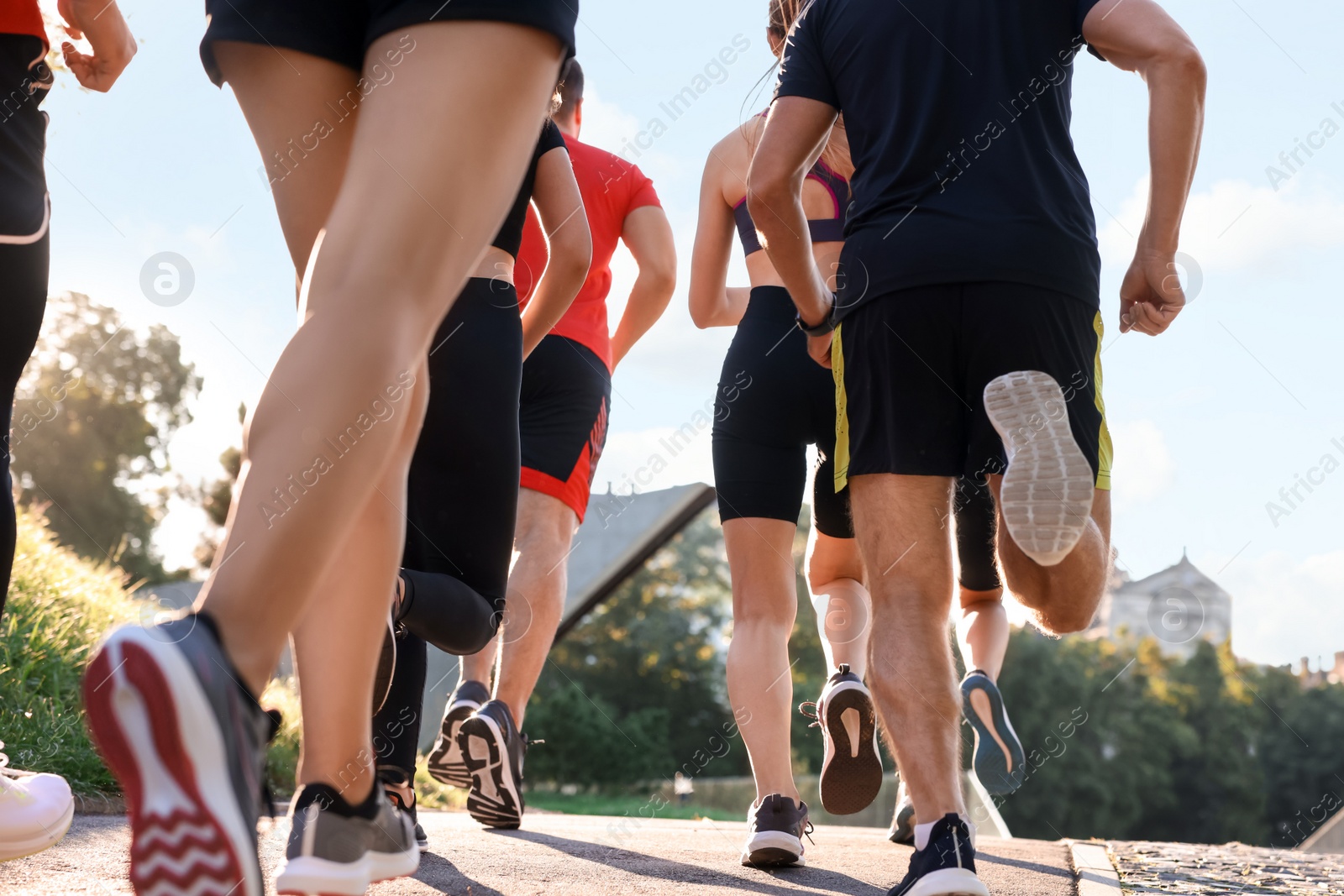 Photo of Group of people running outdoors on sunny day, back view