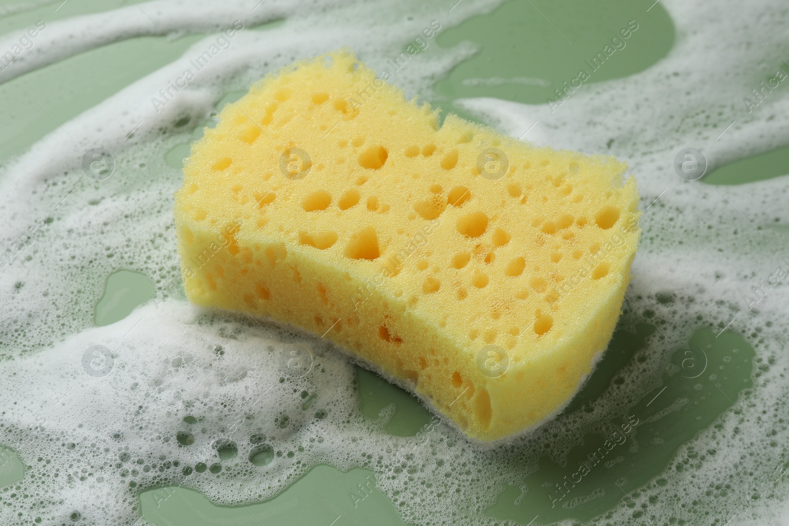 Photo of Yellow sponge with foam on green background, closeup