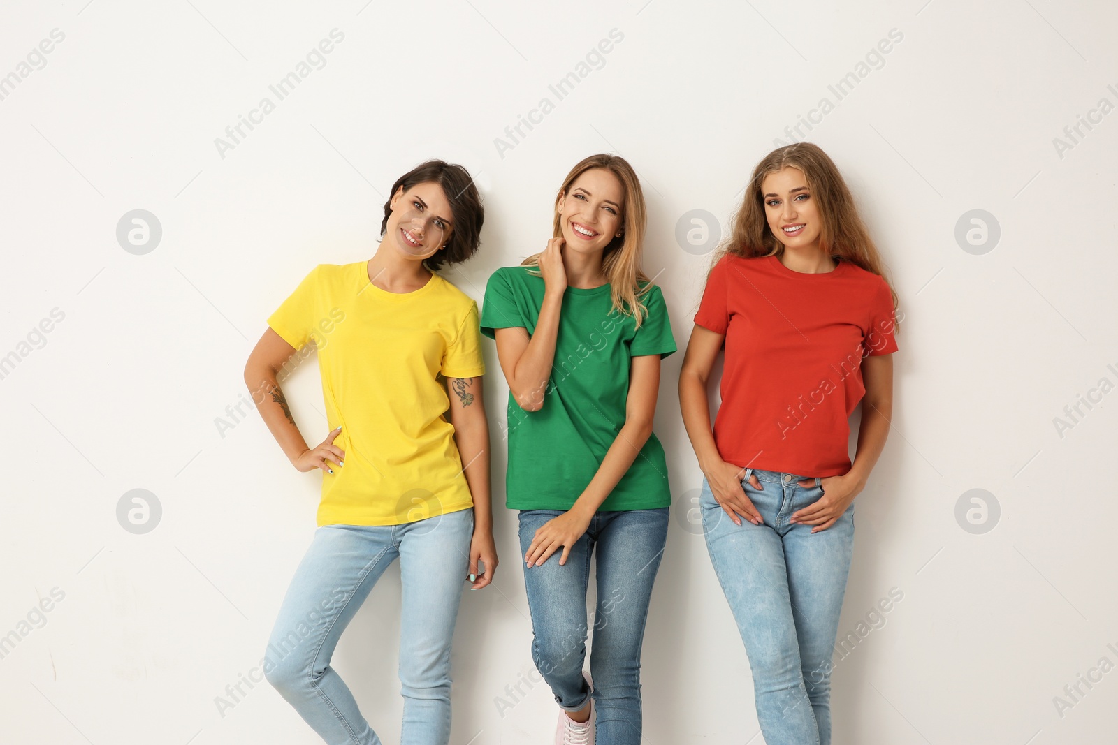 Photo of Group of young women in jeans and colorful t-shirts on light background
