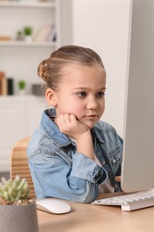 Photo of Little girl using computer at table in room. Internet addiction