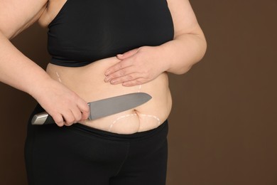 Closeup view of obese woman with knife and marks on body against brown background, space for text. Weight loss surgery