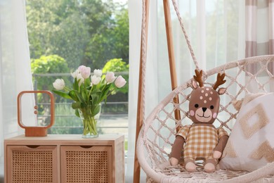 Swing chair with toy reindeer near window indoors. Interior design