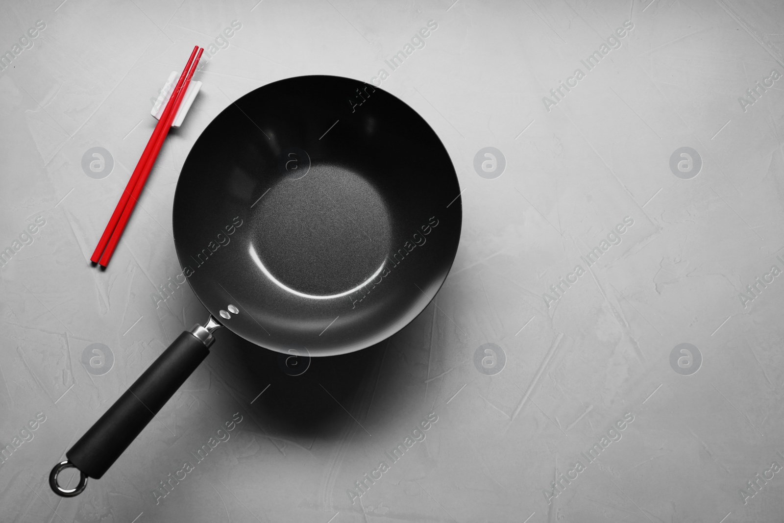 Photo of Empty wok and chopsticks on grey table, flat lay. Space for text