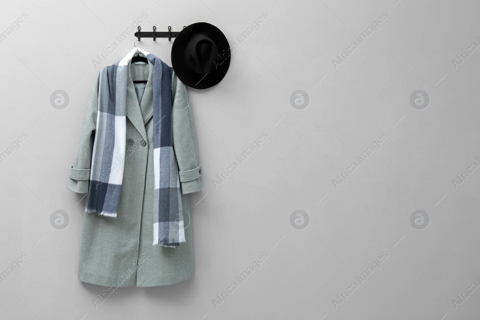 Photo of Hanger with coat, scarf and hat on light grey wall, space for text